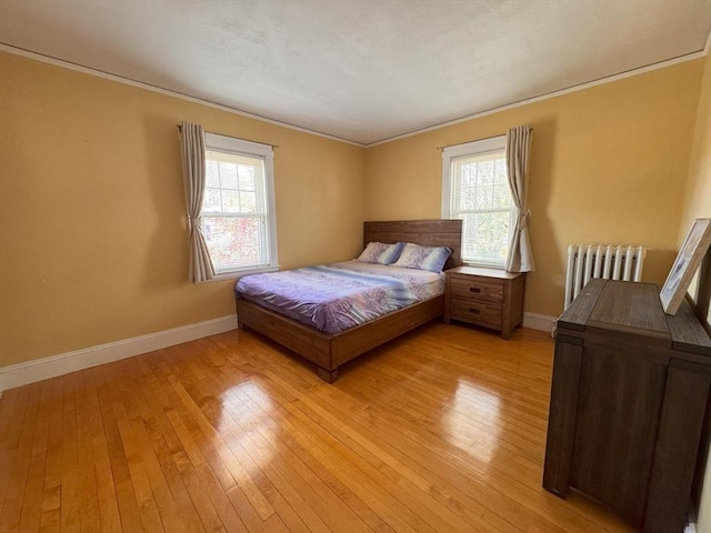 bedroom featuring baseboards, radiator, crown molding, and light wood-style flooring