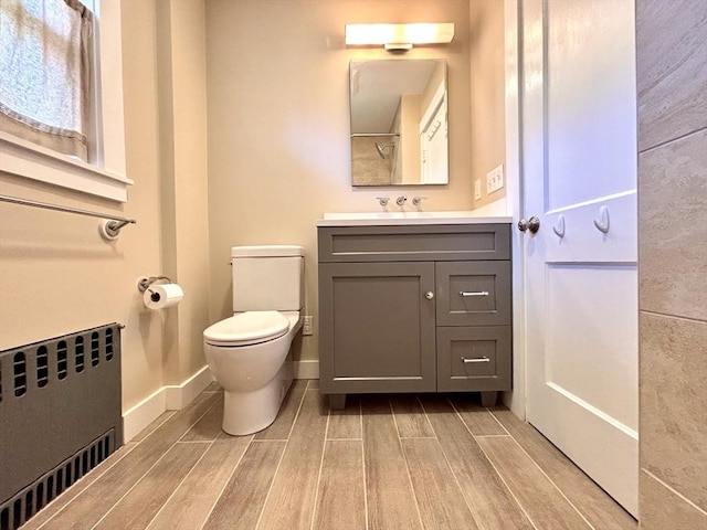 bathroom with wood tiled floor, baseboards, radiator, toilet, and vanity