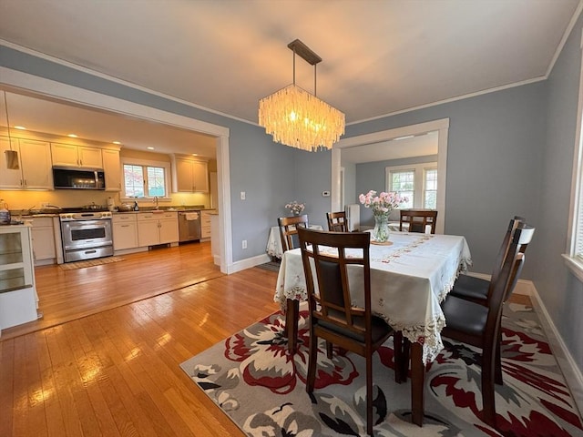 dining space featuring baseboards, a notable chandelier, crown molding, and light wood finished floors