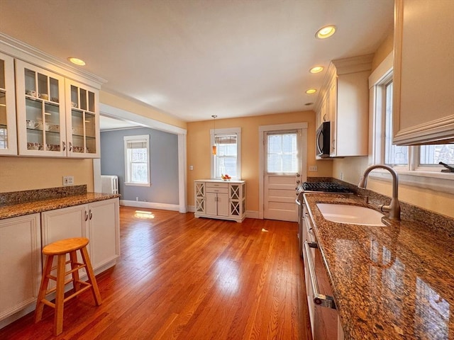 kitchen with glass insert cabinets, a sink, appliances with stainless steel finishes, light wood-type flooring, and recessed lighting