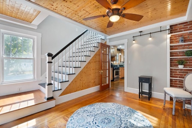 staircase with hardwood / wood-style flooring, ceiling fan, wooden ceiling, and brick wall