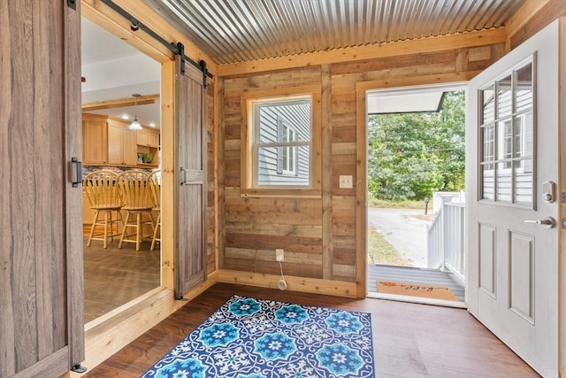 doorway to outside with a barn door, dark hardwood / wood-style floors, and wooden walls