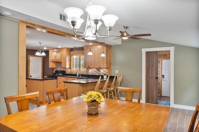 dining room with hardwood / wood-style flooring, ceiling fan with notable chandelier, sink, and vaulted ceiling