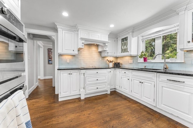 kitchen with a sink, tasteful backsplash, glass insert cabinets, and white cabinets