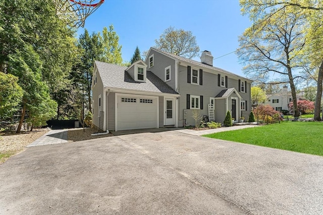 colonial home featuring a chimney, a front yard, aphalt driveway, and an attached garage