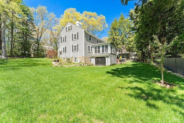 view of property exterior featuring a yard, fence, a sunroom, and a chimney