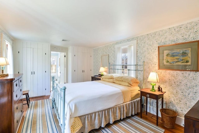 bedroom with wood finished floors, visible vents, multiple windows, and wallpapered walls