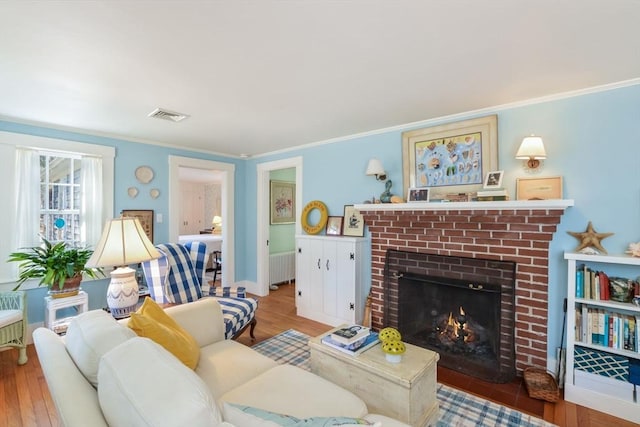 living room with light wood-style flooring, a fireplace, ornamental molding, and visible vents