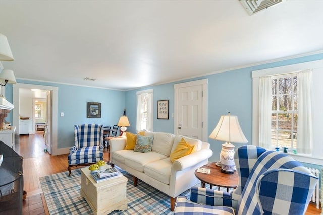 living area with ornamental molding, wood finished floors, visible vents, and baseboards