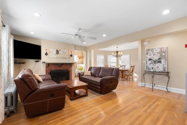 living room with a fireplace, ceiling fan with notable chandelier, and light hardwood / wood-style flooring