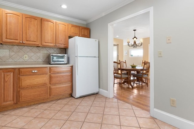 kitchen with tasteful backsplash, light tile patterned floors, ornamental molding, white fridge, and pendant lighting