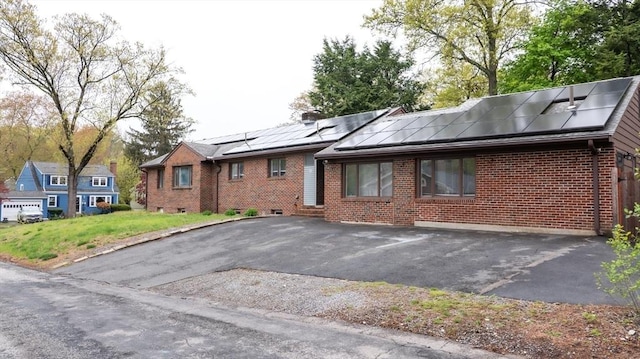 view of front of house featuring brick siding, roof mounted solar panels, and driveway