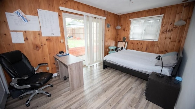 bedroom featuring multiple windows, wooden walls, access to exterior, light wood finished floors, and an office area
