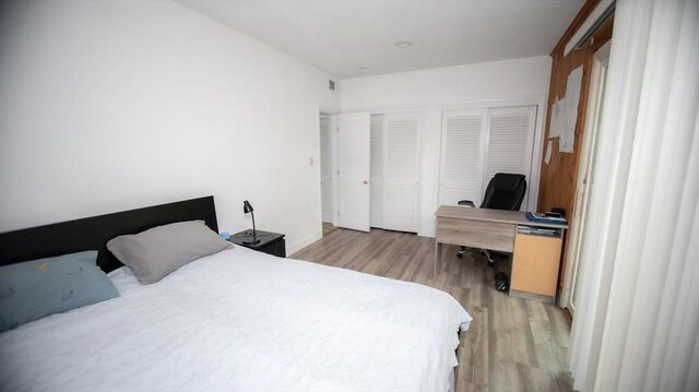 bedroom featuring light wood-style floors, a desk, and multiple closets