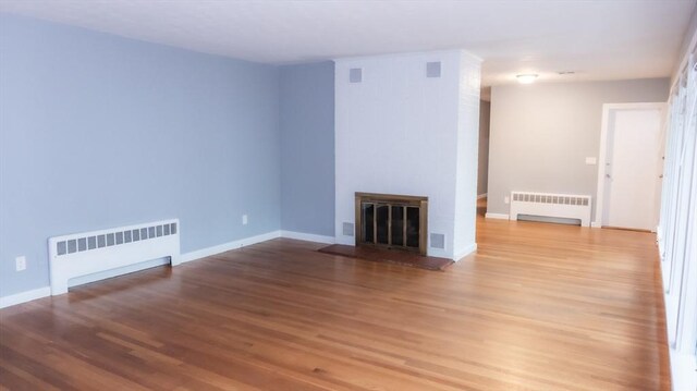 unfurnished living room with radiator heating unit, wood finished floors, and a fireplace