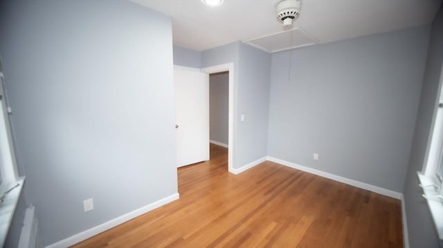 unfurnished room with attic access, light wood-style floors, and baseboards