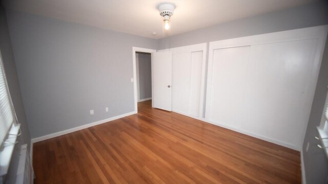 unfurnished bedroom with two closets, wood finished floors, and baseboards