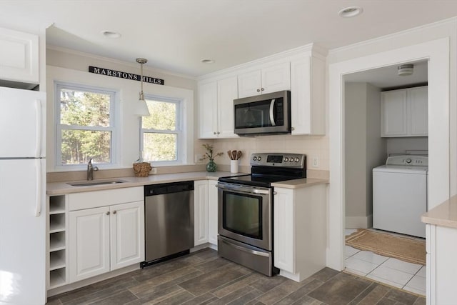 kitchen featuring appliances with stainless steel finishes, washer / clothes dryer, light countertops, white cabinetry, and a sink