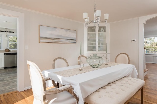 dining room featuring light wood-type flooring, a notable chandelier, arched walkways, and crown molding