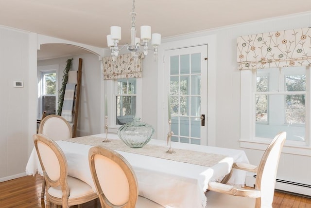 dining space with arched walkways, a notable chandelier, a baseboard heating unit, wood finished floors, and crown molding