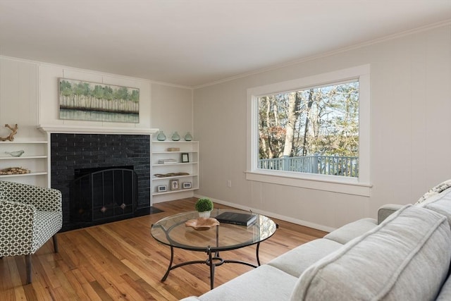 living area with a brick fireplace, ornamental molding, and wood finished floors