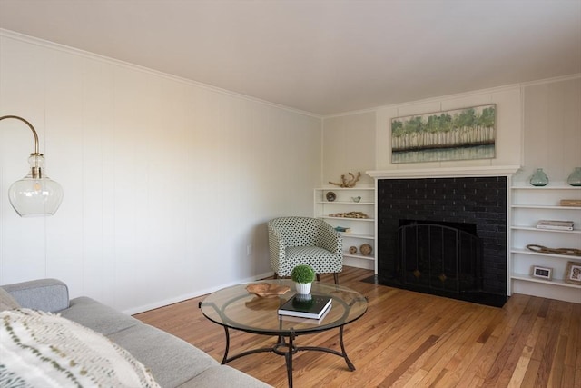 living area with ornamental molding, a fireplace, wood finished floors, and built in shelves