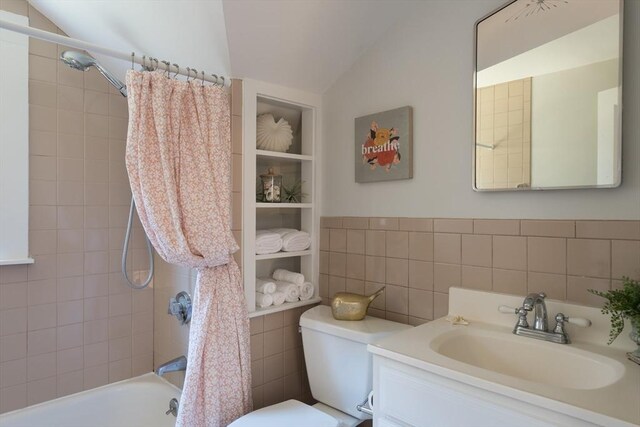 bathroom featuring toilet, vanity, tile walls, vaulted ceiling, and shower / bathing tub combination