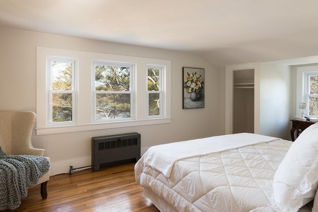 bedroom with radiator heating unit, vaulted ceiling, and wood-type flooring