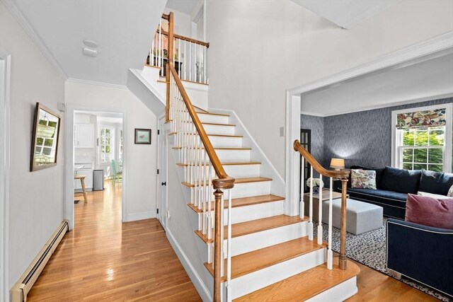 stairs featuring a baseboard radiator, wood finished floors, crown molding, and baseboards