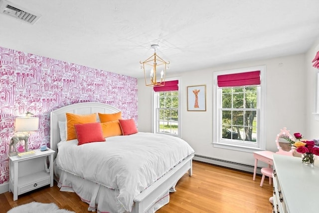 bedroom with a baseboard radiator, a chandelier, wallpapered walls, light wood finished floors, and an accent wall