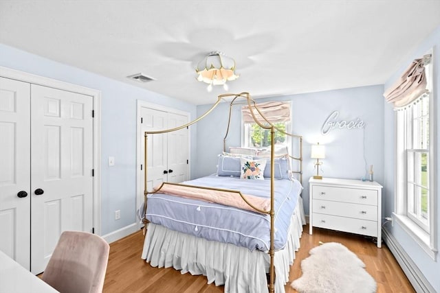 bedroom featuring baseboard heating, multiple windows, wood finished floors, and multiple closets