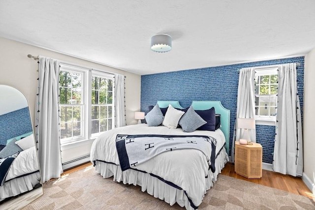 bedroom featuring baseboard heating, multiple windows, and wood finished floors