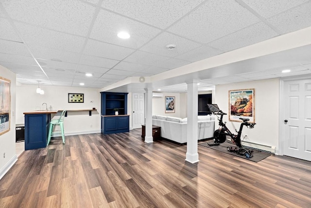 workout area featuring a paneled ceiling, dark wood finished floors, baseboard heating, wet bar, and a wall unit AC