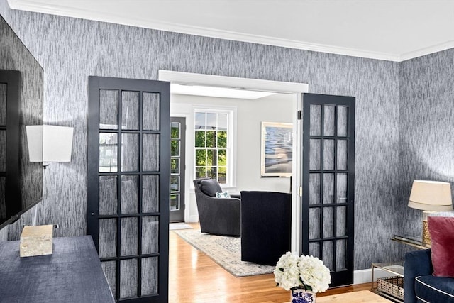 doorway with wallpapered walls, wood finished floors, and ornamental molding