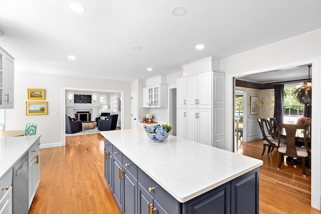 kitchen featuring white cabinetry, a kitchen island, light countertops, a fireplace, and light wood finished floors