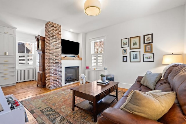 living area featuring baseboards, light wood finished floors, radiator heating unit, and a fireplace