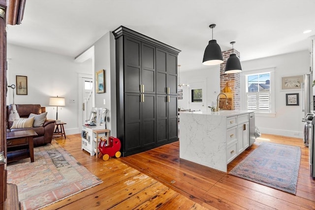 kitchen featuring decorative light fixtures, an island with sink, open floor plan, light stone countertops, and light wood-style floors