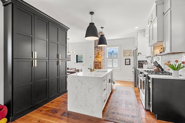 kitchen with light wood-style flooring, an island with sink, a sink, stainless steel appliances, and light stone counters