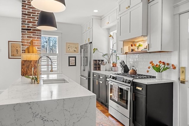 kitchen with dark cabinets, a sink, stainless steel appliances, light stone countertops, and tasteful backsplash