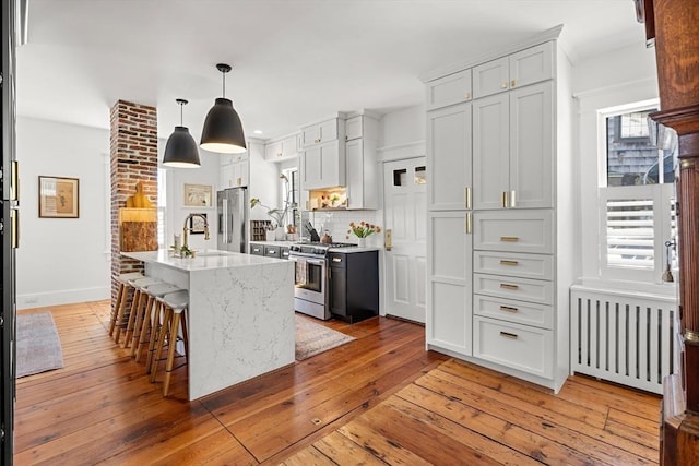 kitchen featuring light wood-style flooring, radiator, light stone counters, a sink, and appliances with stainless steel finishes