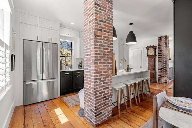 kitchen featuring high end fridge, light wood-style flooring, a kitchen bar, ornate columns, and light countertops