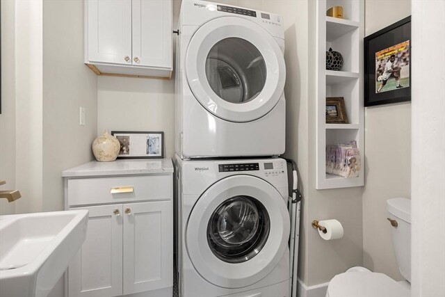 clothes washing area featuring a sink, stacked washing maching and dryer, and cabinet space