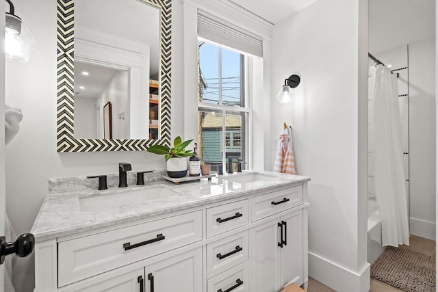 full bath featuring baseboards, shower / bath combo with shower curtain, double vanity, and a sink