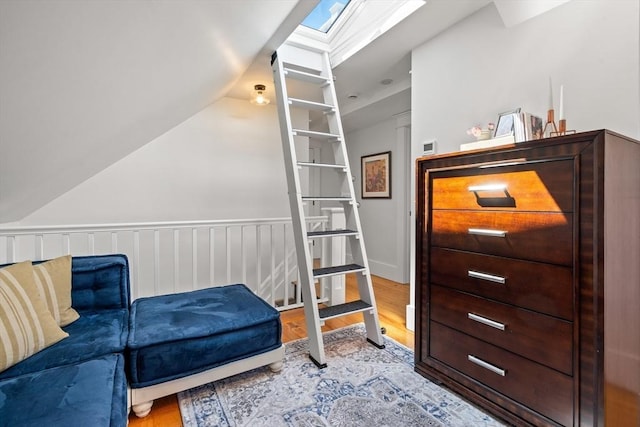 living area with a wainscoted wall, wood finished floors, and vaulted ceiling with skylight
