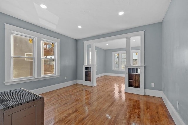 unfurnished living room with ornate columns, heating unit, and light wood-type flooring