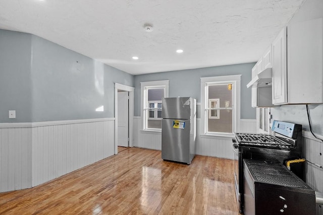 kitchen featuring range with gas cooktop, white cabinets, stainless steel fridge, light hardwood / wood-style floors, and wall chimney range hood