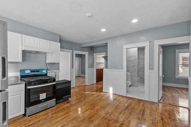 kitchen with white cabinetry, light stone countertops, light wood-type flooring, and stainless steel gas range oven