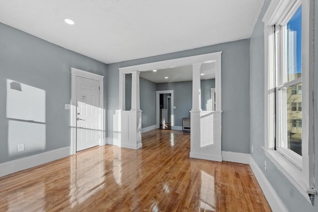 spare room with hardwood / wood-style flooring, decorative columns, and a healthy amount of sunlight