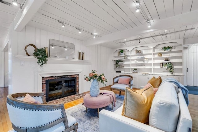 living area featuring a brick fireplace, rail lighting, wood finished floors, and beamed ceiling