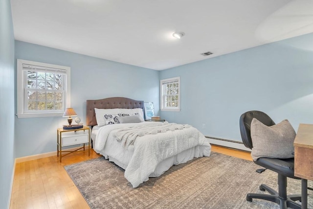 bedroom featuring visible vents, multiple windows, baseboard heating, and hardwood / wood-style flooring